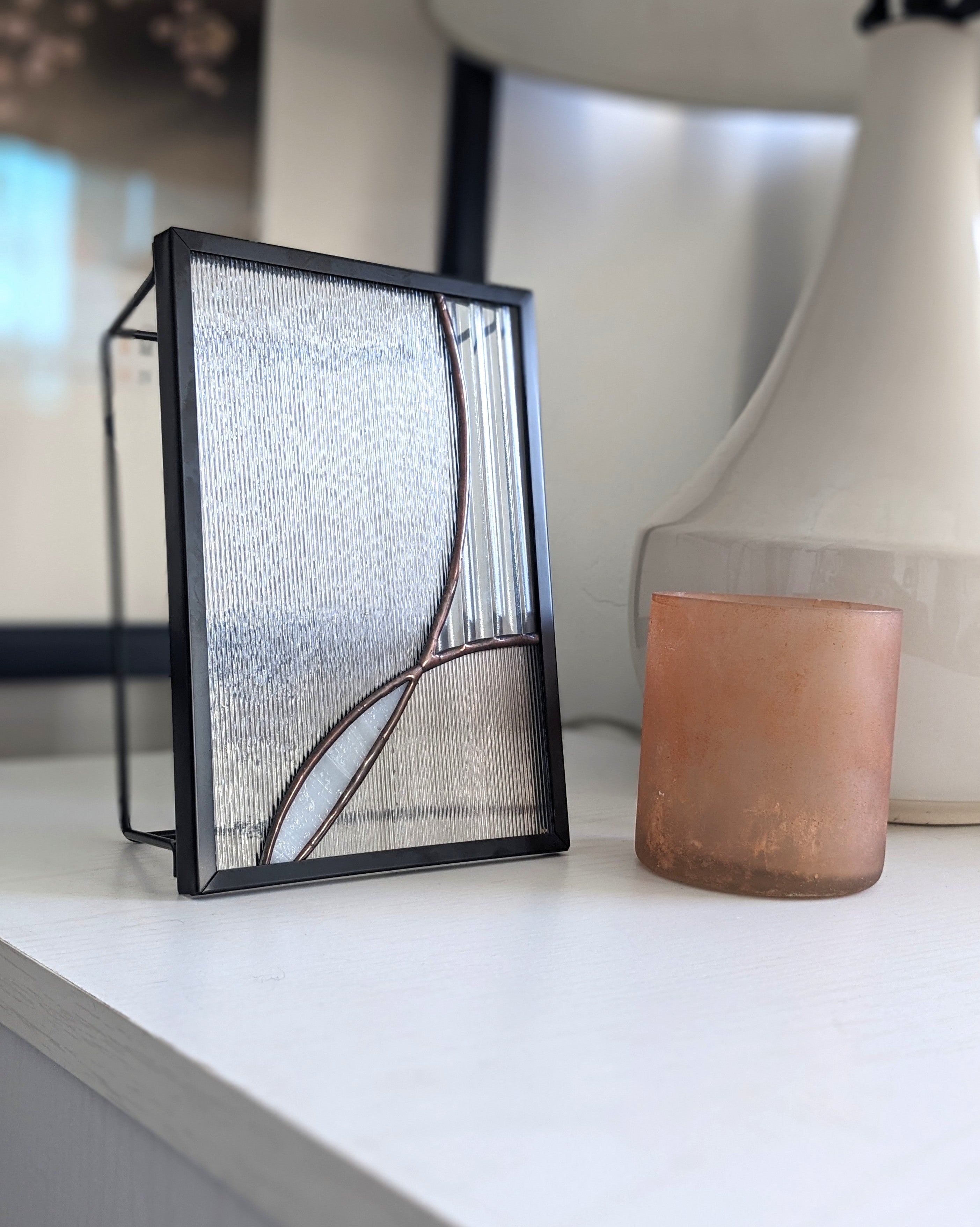 Decorative glass panel with black frame on a white surface, photographed from the left