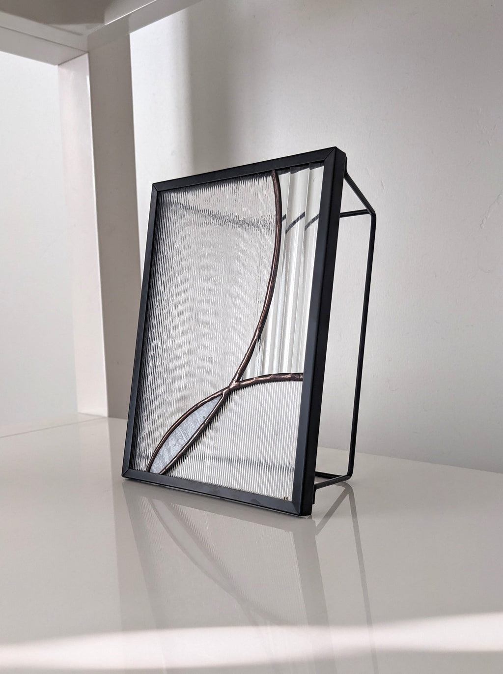 Modern stained glass artwork on a white shelf, photographed from the right.