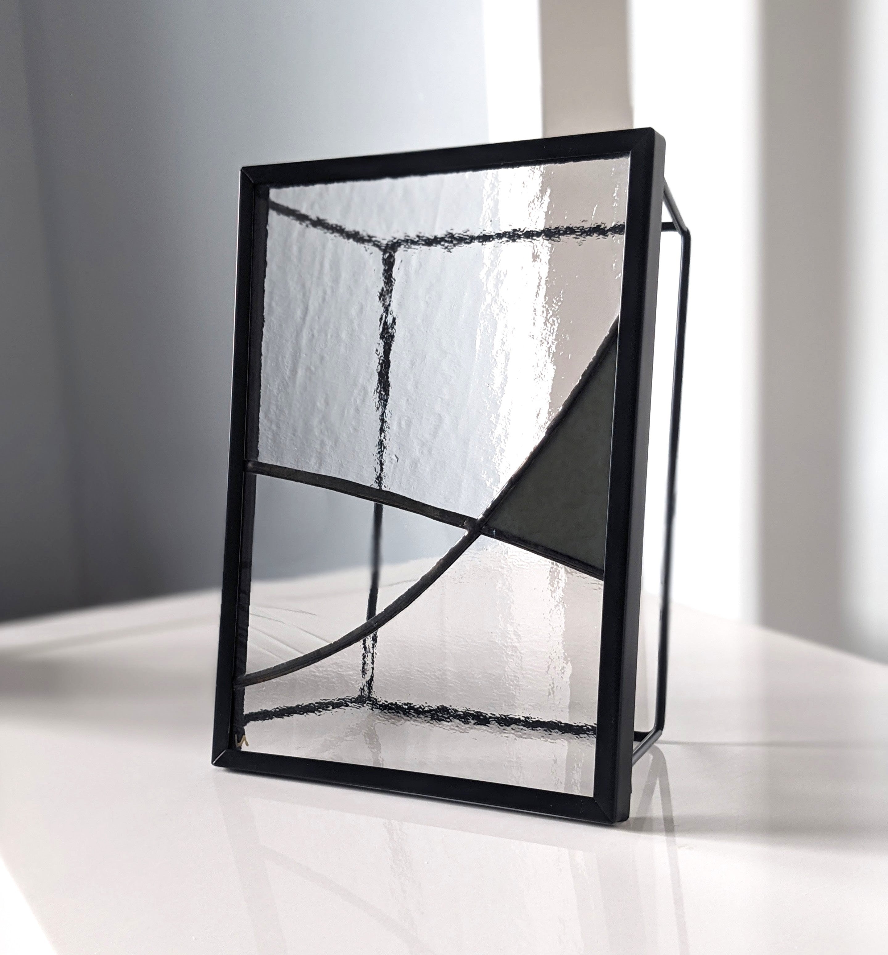 Black-framed glass artwork with green detail on a white with a grey background.