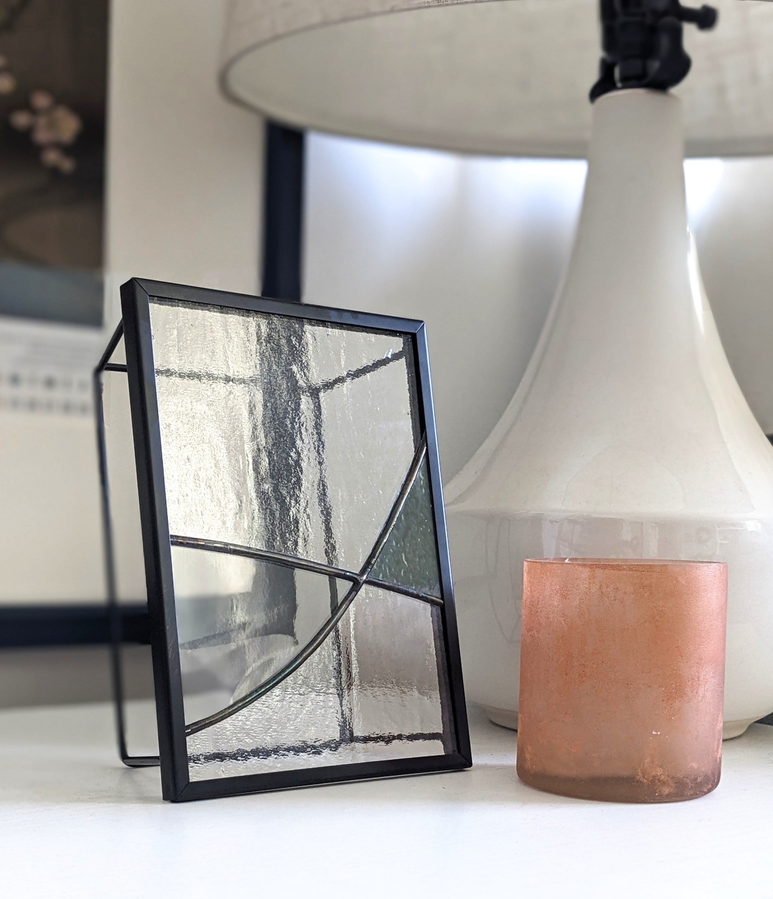 Framed glass artwork on a surface with a lamp and candle in the background