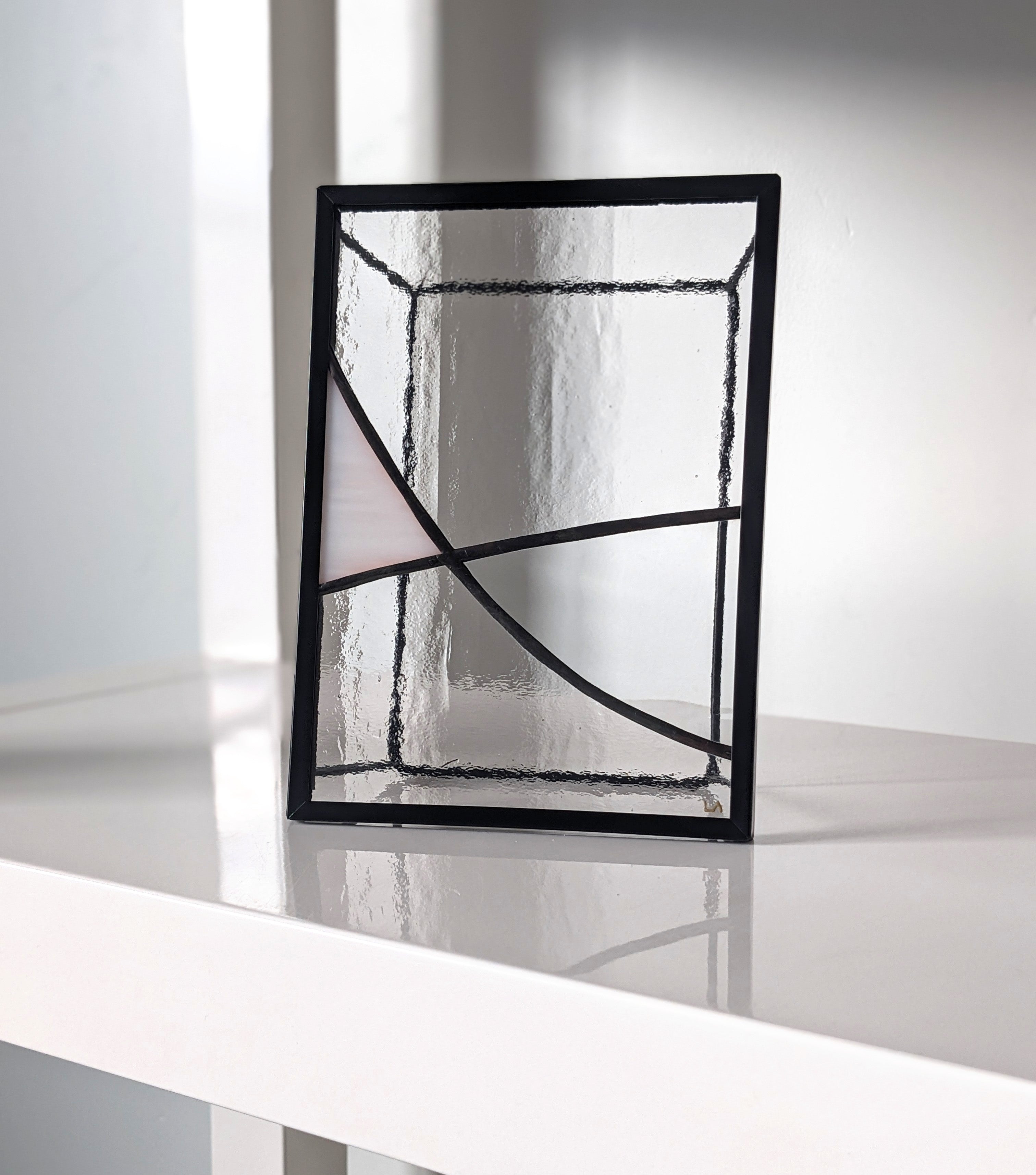 Decorative stained glass art with black frame on a white shelf