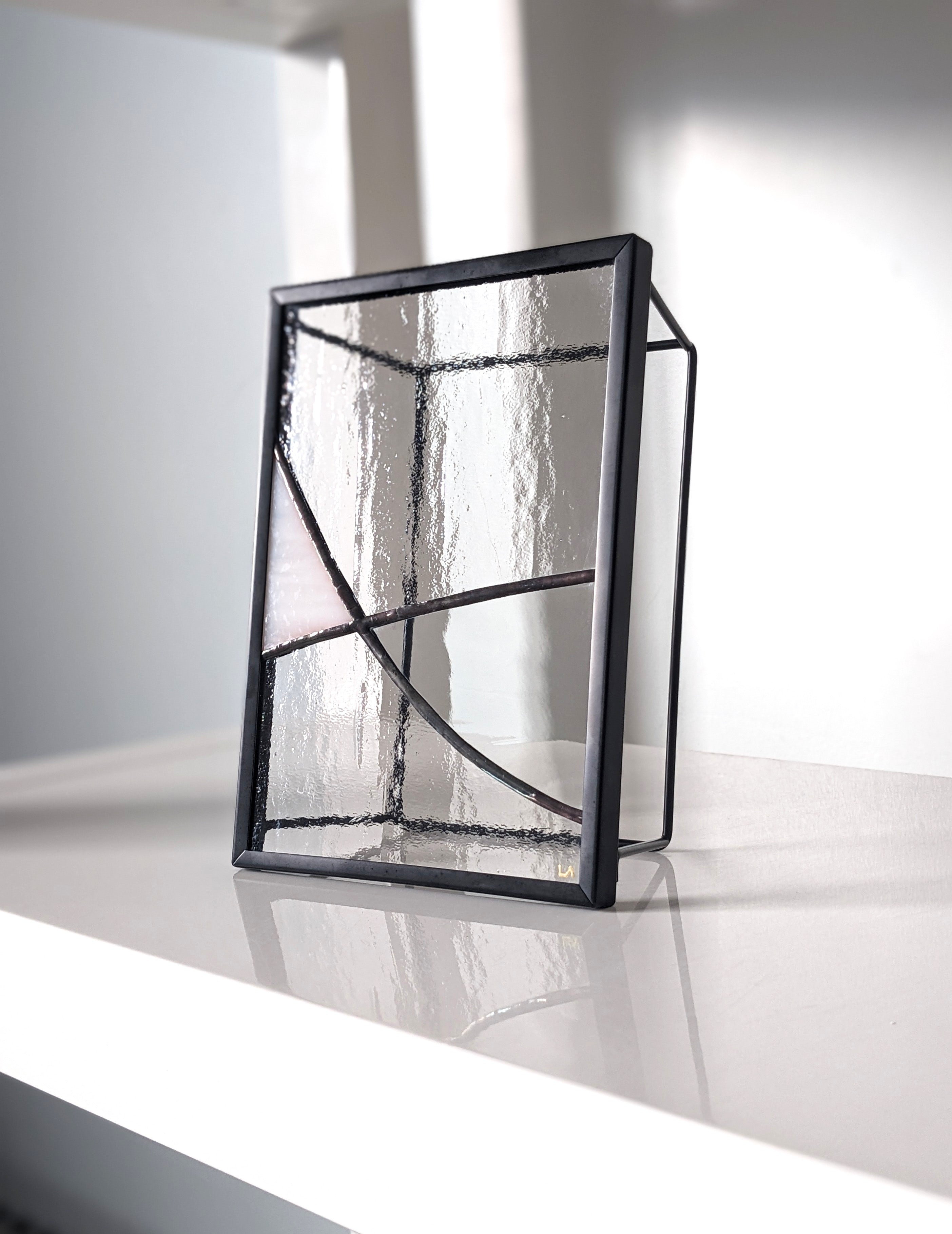 Modern black-framed glass art photographed at an angle on a white shelf.