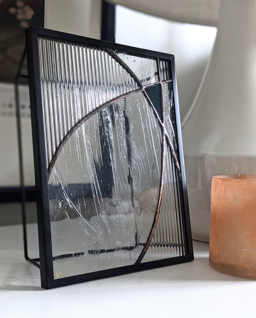 Textured glass artwork in a black frame on a white surface with a blurred background.