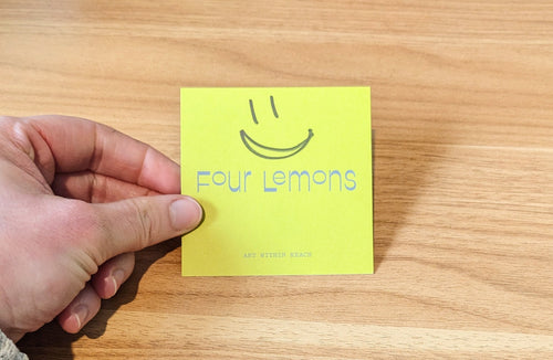Hand holding a yellow card with 'Four Lemons' logo on a wooden surface