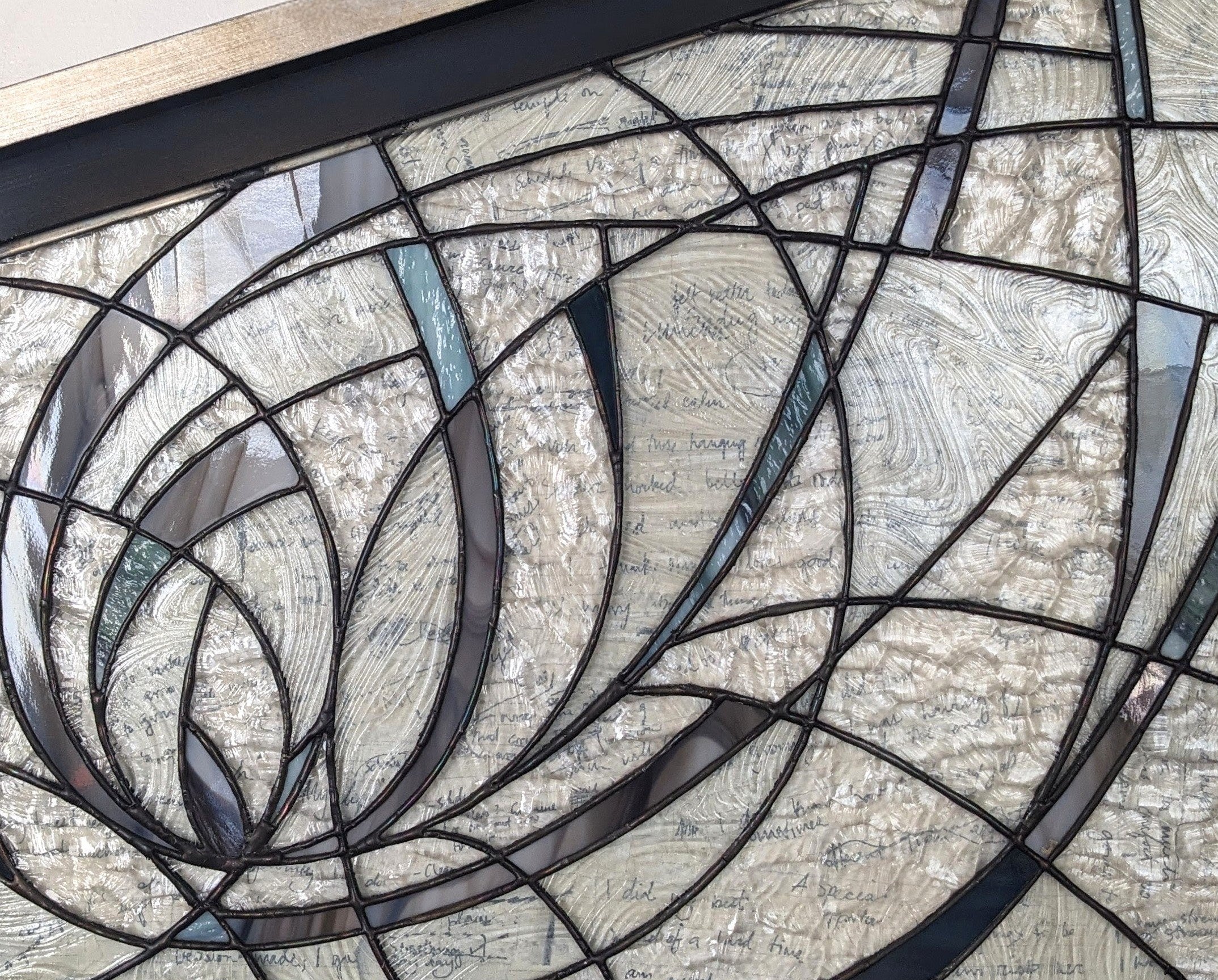 Close up of stained glass artwork with curving lines and hand-written notes behind the glass